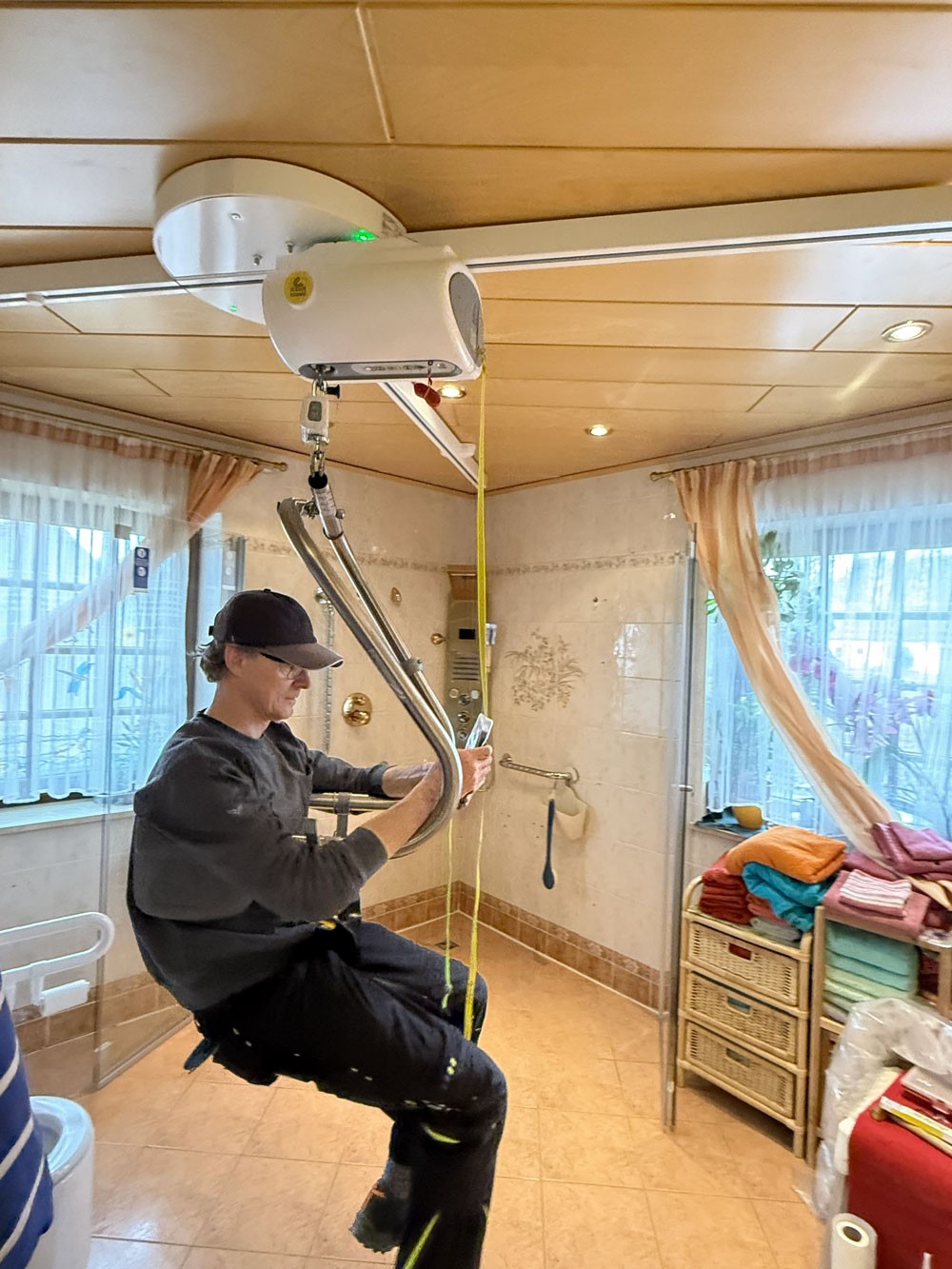 Unser Berater hängt im Hebebügel und bewegt den Deckenmotor mit der Fernbedienung Richtung Dusche.