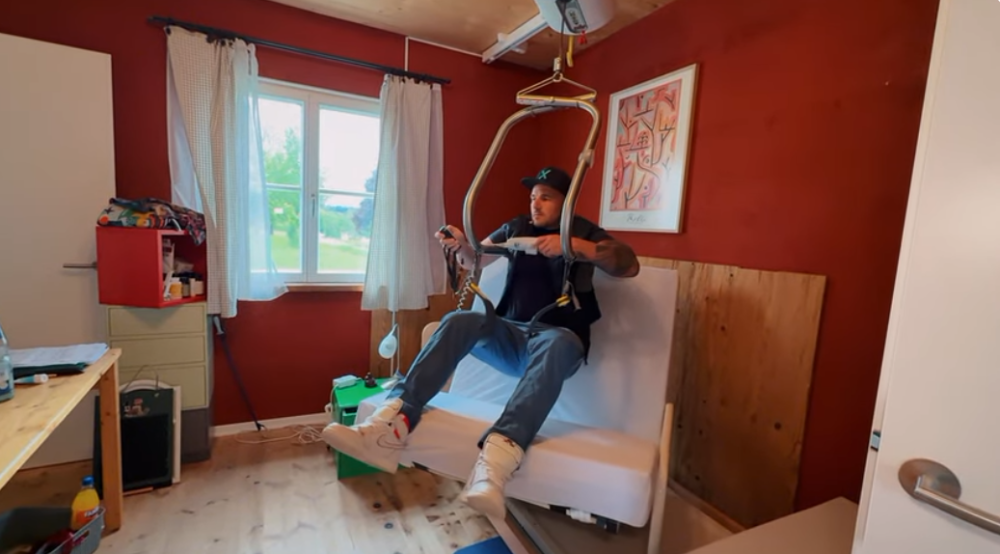 Daniel Schöb, der Hilfsmittelberater, zeigt wie der Deckenlifter funktioniert. Er schwebt über einer Liege.