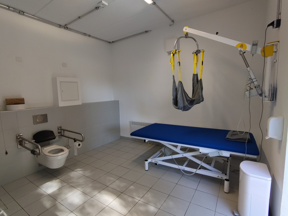 Toilette für alle mit Wandlifter und Hebetuch über einer Pflegeliege